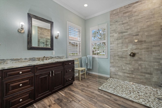 full bath with ornamental molding, vanity, wood finished floors, tiled shower, and baseboards