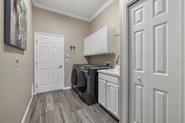 washroom with crown molding, light wood finished floors, cabinet space, washing machine and dryer, and baseboards