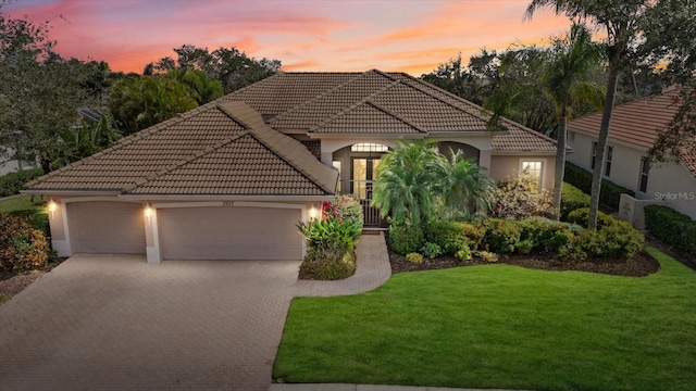 mediterranean / spanish-style home featuring a garage, a tiled roof, decorative driveway, a yard, and stucco siding