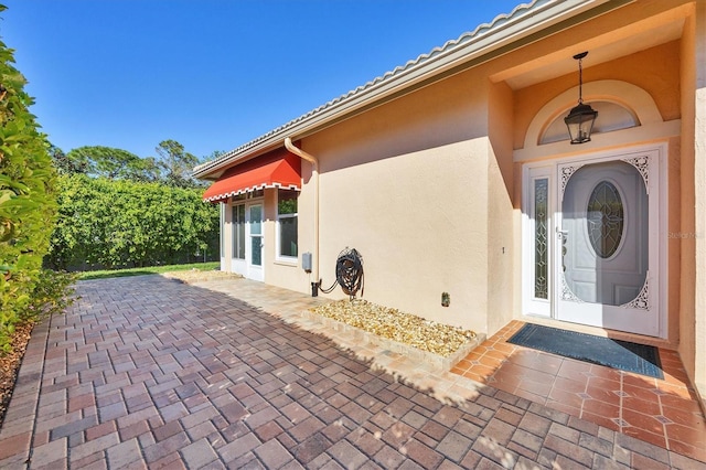 property entrance featuring stucco siding, a tile roof, and a patio