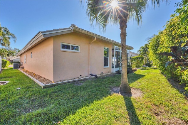 view of side of home featuring a yard, cooling unit, and stucco siding