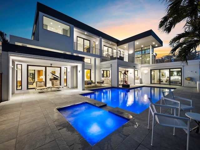 back of house with a patio, a pool with connected hot tub, a balcony, and stucco siding