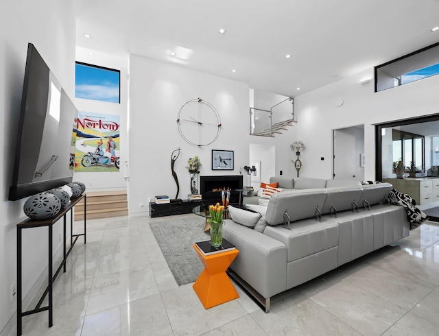 living room featuring a warm lit fireplace, marble finish floor, a towering ceiling, and recessed lighting