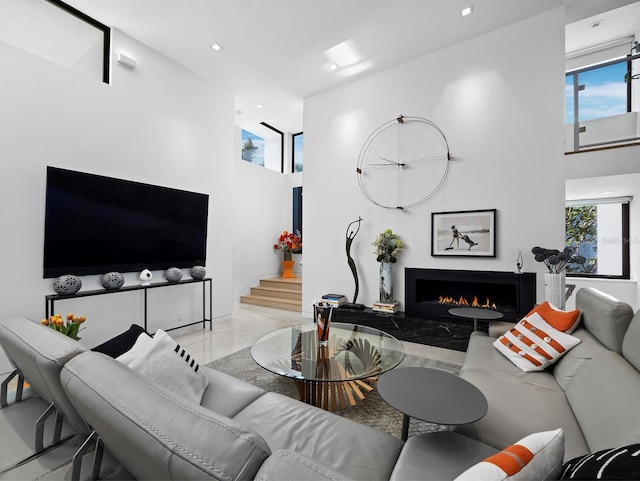 living area with marble finish floor, recessed lighting, stairway, a high ceiling, and a lit fireplace