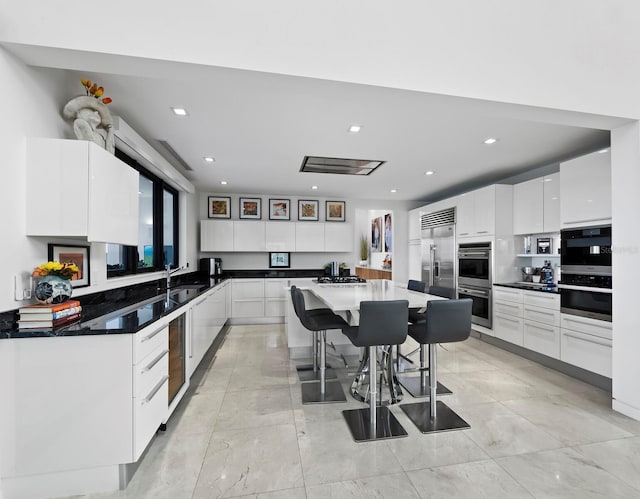 kitchen with stainless steel appliances, a sink, white cabinetry, a kitchen breakfast bar, and a center island