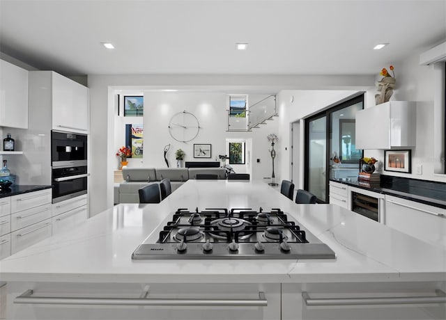 kitchen with wine cooler, stainless steel gas cooktop, a large island, recessed lighting, and white cabinets