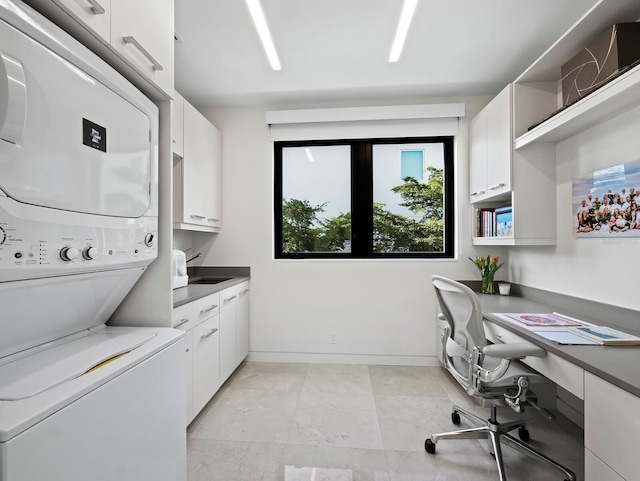 laundry room with baseboards, cabinet space, a sink, and stacked washing maching and dryer