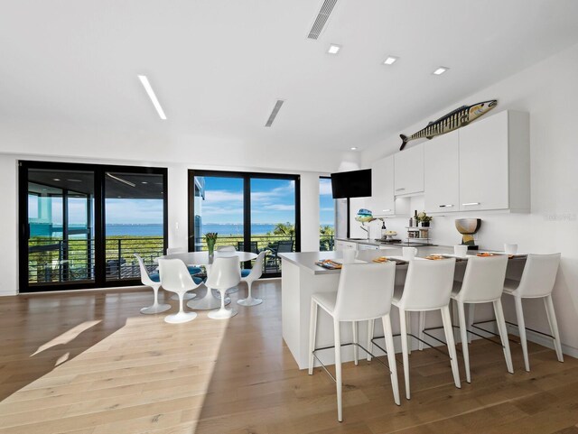 kitchen with a breakfast bar, visible vents, white cabinetry, wood finished floors, and a peninsula