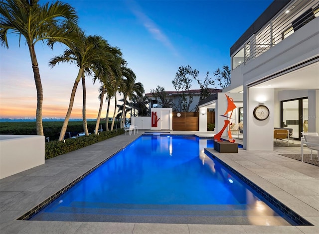 pool at dusk featuring fence, a fenced in pool, and a patio