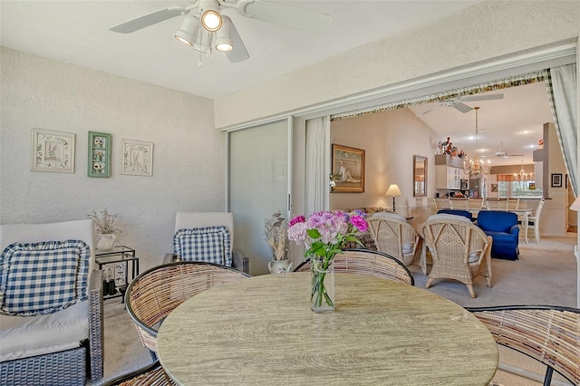 dining room with light carpet, a textured wall, a ceiling fan, and lofted ceiling