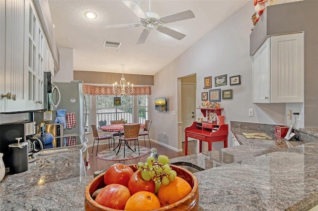 kitchen featuring lofted ceiling, visible vents, stone countertops, white cabinetry, and a textured ceiling