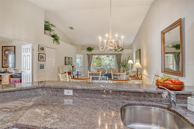 kitchen with high vaulted ceiling, stone countertops, a sink, and an inviting chandelier