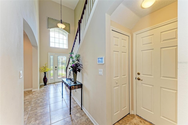 foyer with arched walkways, light tile patterned floors, a towering ceiling, and baseboards