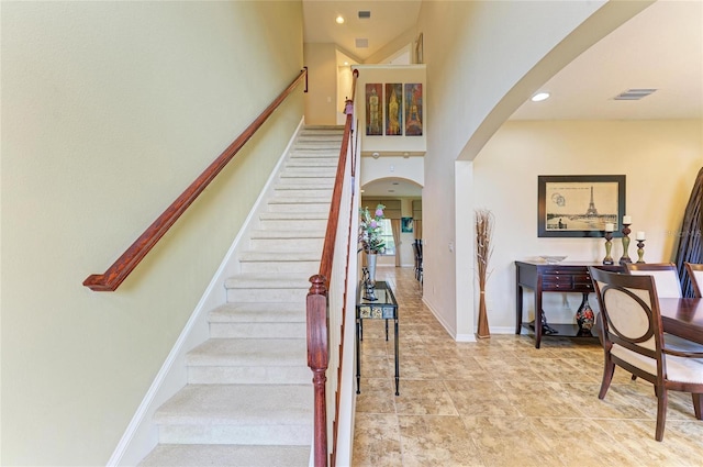 staircase with arched walkways, recessed lighting, a high ceiling, visible vents, and baseboards