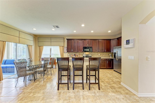 kitchen with visible vents, decorative backsplash, baseboards, appliances with stainless steel finishes, and a kitchen bar