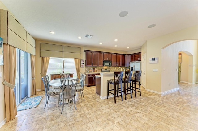 kitchen with arched walkways, a breakfast bar area, stainless steel appliances, light countertops, and backsplash