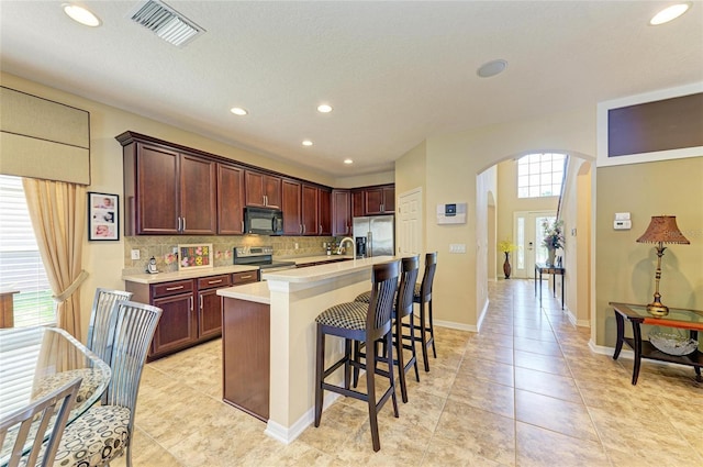 kitchen with tasteful backsplash, visible vents, arched walkways, appliances with stainless steel finishes, and light countertops