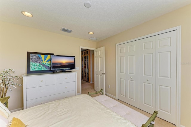 bedroom with a closet, light colored carpet, visible vents, a textured ceiling, and baseboards