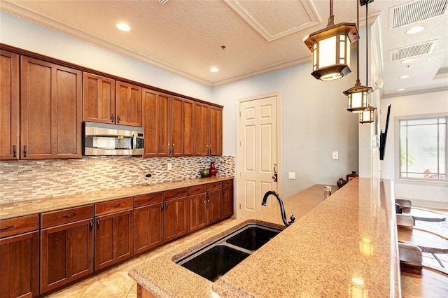 kitchen with stainless steel microwave, a sink, visible vents, and decorative backsplash