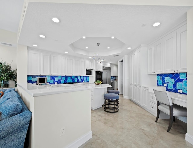 kitchen featuring a kitchen bar, black appliances, a tray ceiling, white cabinets, and light countertops