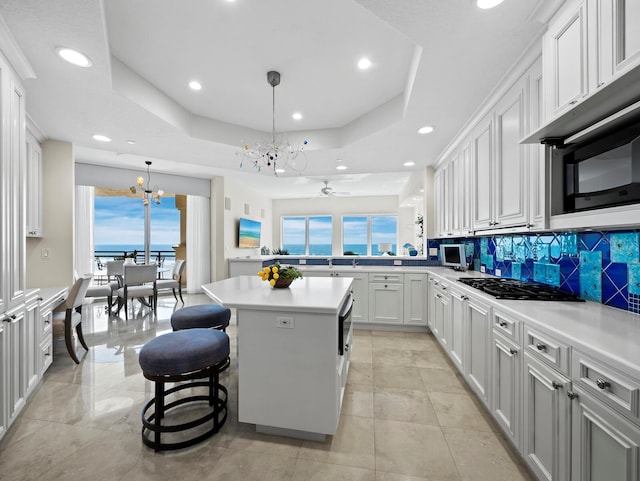 kitchen featuring light countertops, black gas cooktop, a raised ceiling, backsplash, and a center island