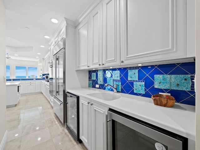 kitchen with beverage cooler, appliances with stainless steel finishes, white cabinetry, and a sink