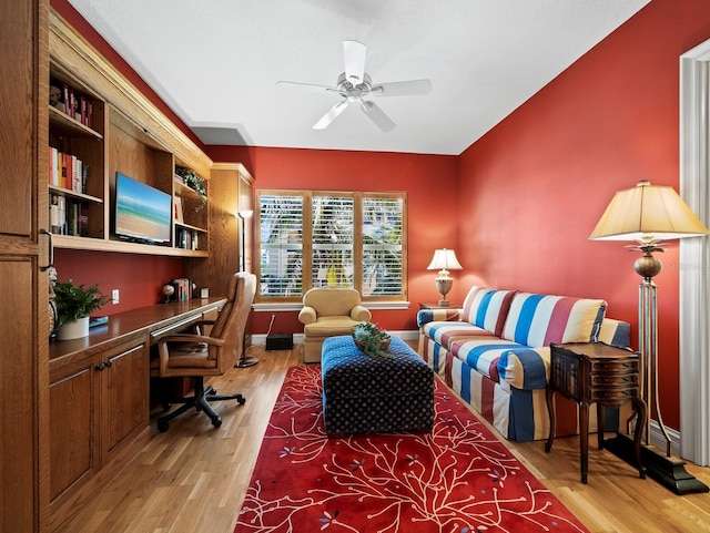 office area featuring a ceiling fan, baseboards, light wood finished floors, and built in desk