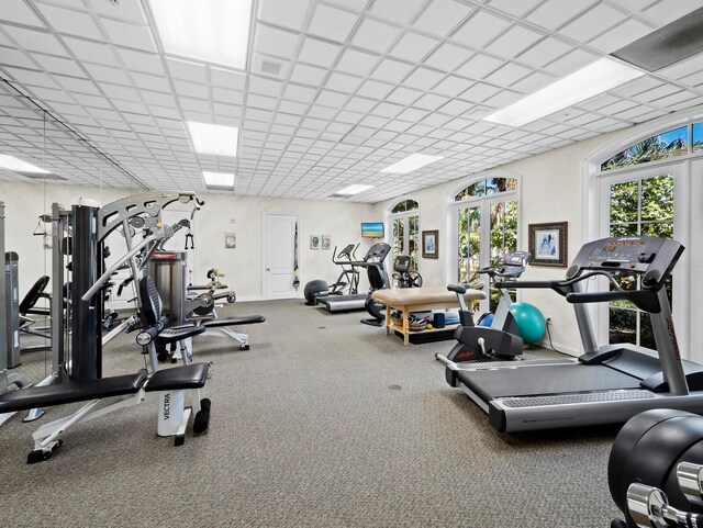 exercise room featuring visible vents, a paneled ceiling, and baseboards