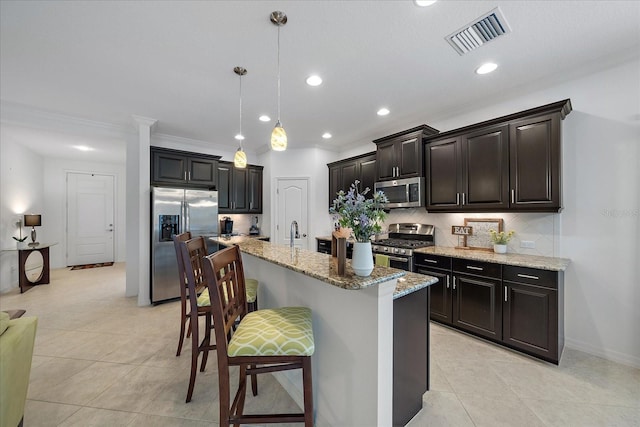 kitchen featuring light stone counters, stainless steel appliances, tasteful backsplash, visible vents, and a kitchen bar