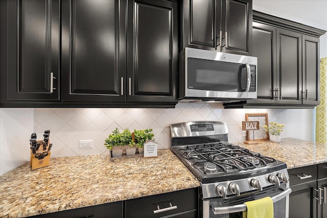 kitchen featuring backsplash, light stone counters, stainless steel appliances, and dark cabinetry