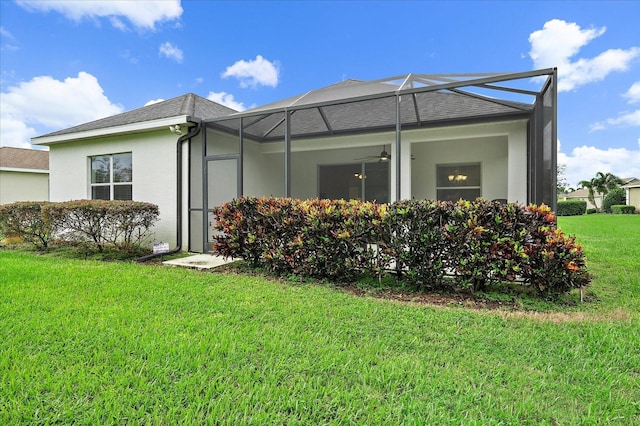 view of side of property featuring ceiling fan, a lanai, a shingled roof, a lawn, and stucco siding