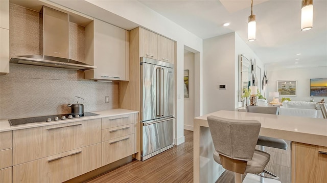 kitchen featuring wall chimney exhaust hood, light brown cabinets, and built in fridge