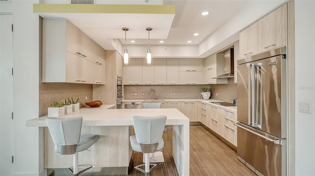 kitchen with a peninsula, wall chimney range hood, modern cabinets, and high end fridge