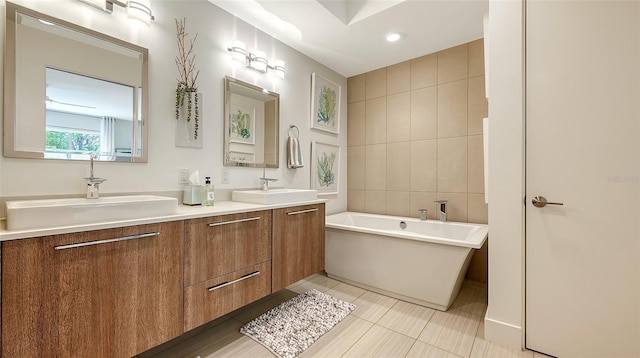 full bath with a sink, tile walls, a freestanding bath, and double vanity