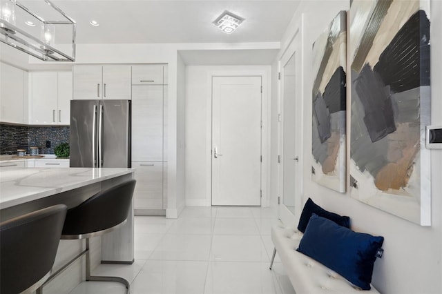 kitchen with light tile patterned floors, light stone counters, white cabinets, freestanding refrigerator, and tasteful backsplash