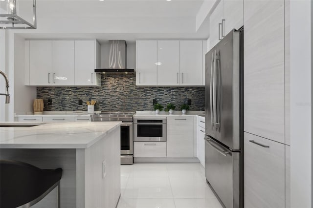 kitchen featuring white cabinets, wall chimney range hood, tasteful backsplash, and stainless steel appliances