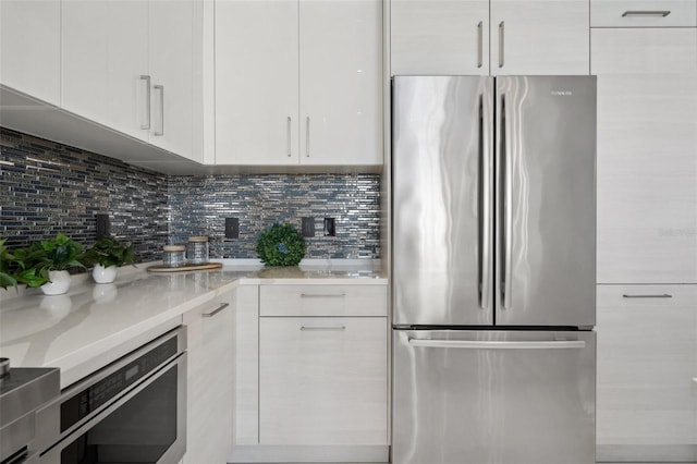 kitchen with tasteful backsplash, white cabinets, light countertops, and freestanding refrigerator