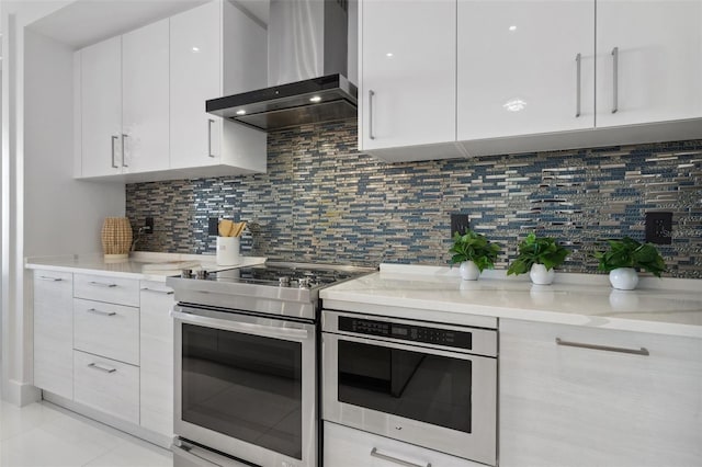 kitchen featuring tasteful backsplash, white cabinets, stainless steel range with electric cooktop, and wall chimney exhaust hood