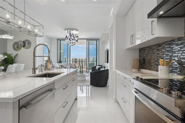 kitchen featuring stainless steel appliances, a sink, backsplash, floor to ceiling windows, and wall chimney exhaust hood