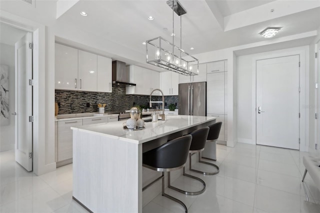 kitchen featuring wall chimney range hood, modern cabinets, freestanding refrigerator, and tasteful backsplash