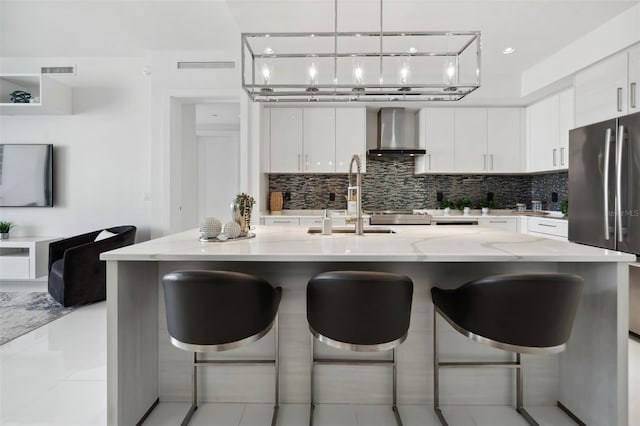 kitchen featuring a sink, white cabinets, wall chimney range hood, backsplash, and freestanding refrigerator