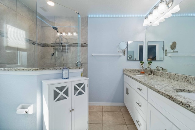 bathroom featuring baseboards, double vanity, a tile shower, a sink, and tile patterned flooring