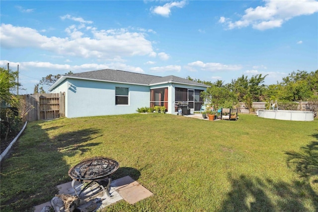 rear view of property featuring a fenced backyard, a sunroom, stucco siding, a fire pit, and a lawn