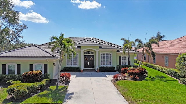 view of front facade with a front yard, a tile roof, and stucco siding