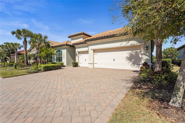 mediterranean / spanish home with a tile roof, decorative driveway, an attached garage, and stucco siding