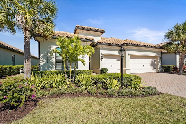 mediterranean / spanish-style home featuring decorative driveway, a tile roof, an attached garage, and stucco siding