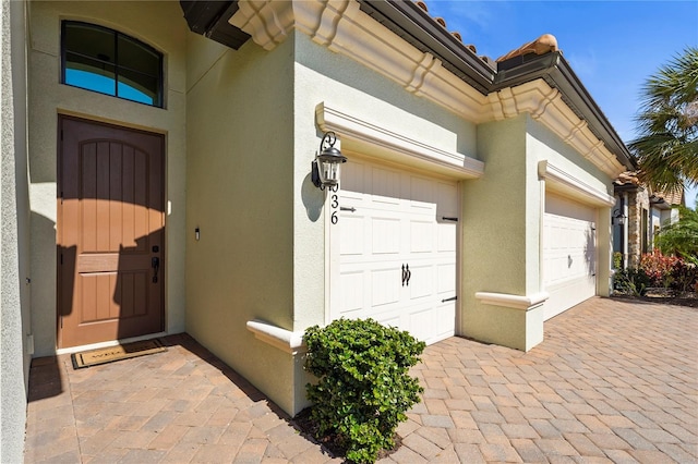 entrance to property with stucco siding, decorative driveway, and an attached garage