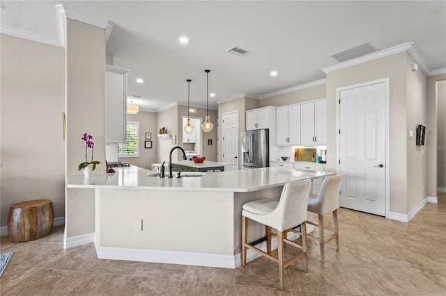 kitchen with visible vents, ornamental molding, stainless steel fridge, white cabinetry, and a sink