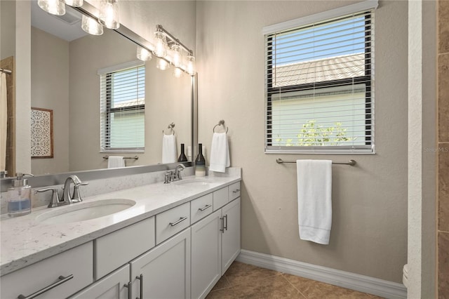 full bath with tile patterned floors, double vanity, baseboards, and a sink