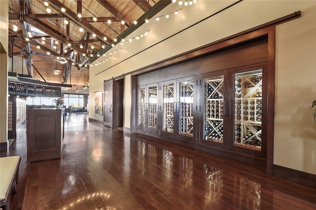 wine area with high vaulted ceiling, dark wood finished floors, a barn door, beamed ceiling, and wooden ceiling